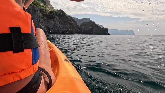 Kayaking, sea, adventure. Person paddling orange kayak on calm water near rocky cliffs, exploring nature.