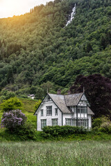 White wooden abandoned house under high waterfall and green mount