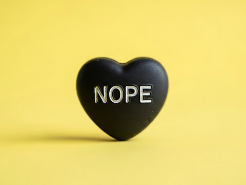A single black heart-shaped candy with the word "nope" on it sits against a bright yellow background, perfect for anti-valentine's day.