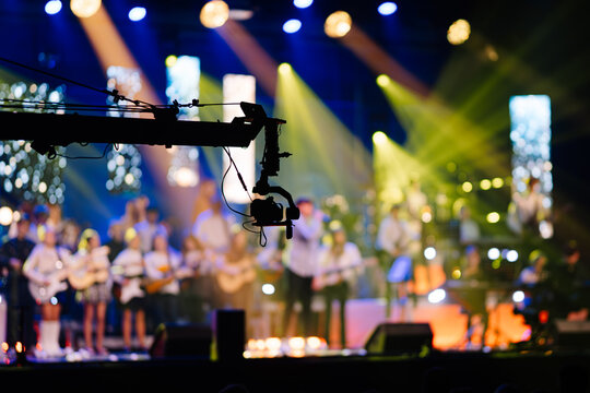 Camera crane captures vibrant live music performance with musicians playing various instruments on stage, illuminated by colorful lights creating an energetic atmosphere