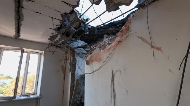 Extensive structural damage to a residential building featuring holes in the roof and ceilings, blown-out doors, and shrapnel marks on walls after an airstrike