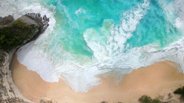 Aerial top-down view of turquoise ocean waves crashing on golden sand at Kelingking Beach, Nusa Penida Island, Bali, Indonesia. Perfect for travel, nature, summer, and tropical paradise themes.