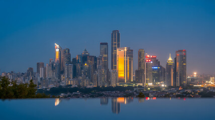 Obraz premium Stunning Cityscape at Dusk with Glowing Skyscrapers and Reflections in Water, Featuring Modern Architecture and a Vibrant Urban Scene in the Evening Light