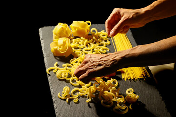 Hands arranging traditional Italian dry pasta on slate board with dramatic lighting