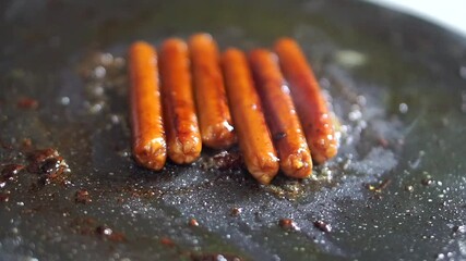 Sausages grilled on a hot pan with sizzling oil, showing the cooking process of fast food.