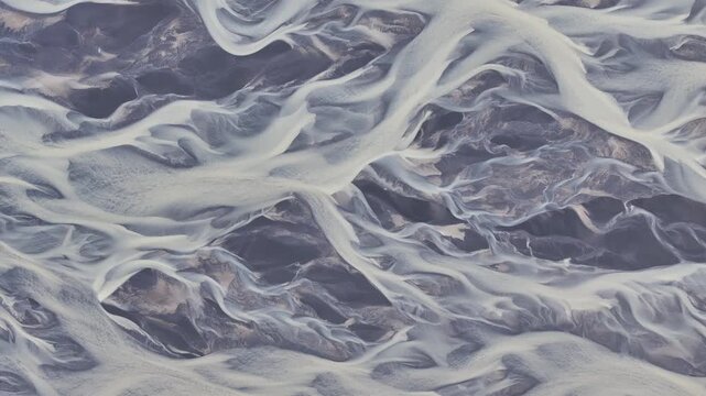 Aerial view of an intricate braided river system carving through the landscape, creating a mesmerizing pattern of contrasting colors, highlands, Iceland.