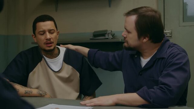 Two men sitting at a table inside the prison, one is comforting the other with a hand on his shoulder Stock Video