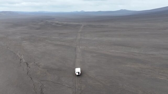 Aerial view of a white camper van driving through a desolate landscape, the dark ground contrasting with the vehicle, highlands, Iceland.