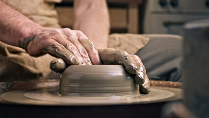A craftsperson shapes clay on a pottery wheel, their hands skillfully molding the material. The setting suggests a workshop, emphasizing creativity and artistry in pottery making.