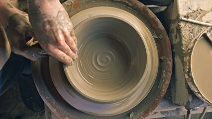 A craftsperson's hands skillfully shape clay on a pottery wheel, creating a smooth, symmetrical...
