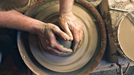 A craftsperson's hands skillfully shape clay on a pottery wheel in a workshop, highlighting creativity and craftsmanship. The spinning wheel and wet clay showcase the transformation of raw materials.