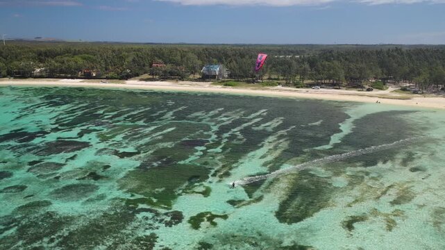 Aerial view of a boat creating a white wake on turquoise waters, with a red parasail visible near the beach, tropical paradise, Mauritius.