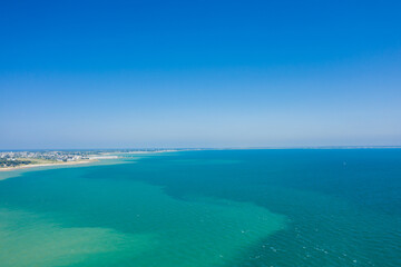 Obraz premium Aerial view of a vast turquoise bay meeting a sandy shoreline near Quiberon, with clear blue skies and distant coastal settlements visible. The scene is sunlit and expansive, evoking a sense of