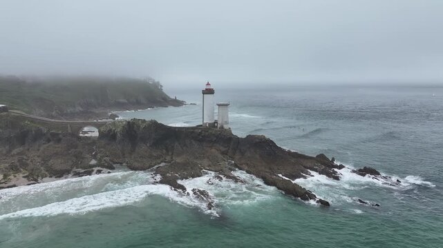 Aerial view of the Petit Minou lighthouse standing tall on a rocky outcrop as waves crash, under a cloudy sky, Bretagne, France.