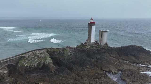 Aerial view of Petit Minou Lighthouse on a craggy rock formation with the bridge and turquoise ocean under an overcast sky, Bretagne, France.