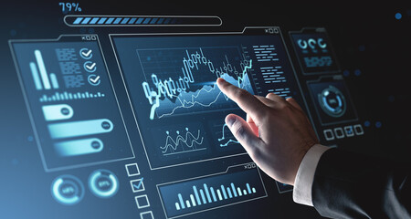 Businessman interacting with futuristic hologram interface displaying financial data and digital charts on a dark blue background. Concept of analytics.