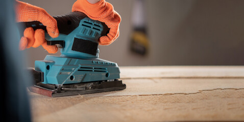 Close up of male hands using a vibration orbital sander to smooth a wooden board surface. Wood finishing process and DIY home improvement concept