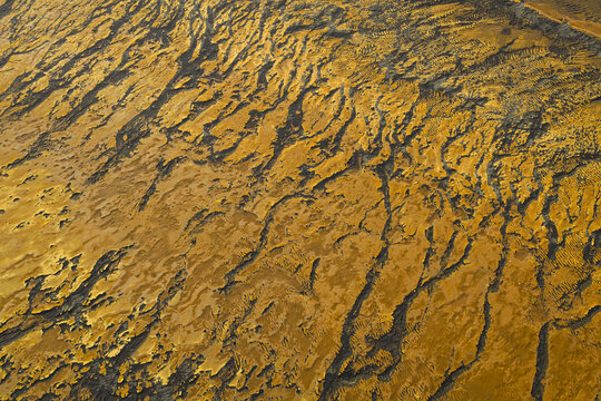 Aerial view of stark, ochre-colored earth etched with dark, winding rivulets creates a textured tapestry under the Icelandic sky, southern Iceland, Iceland.