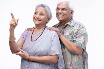 Portrait of happy senior husband embracing wife while standing against white background