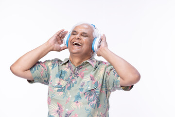 Senior man listening music over headphones and looking up against white background