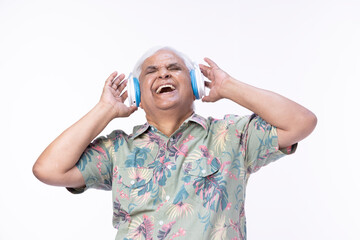 Senior man listening music over headphones and looking up against white background