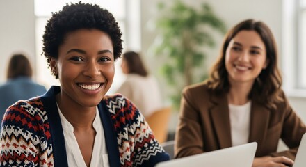 Professional diverse women smiling and working together in modern office environment with laptops and natural light for teamwork collaboration and business success