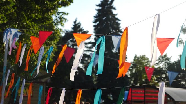 Colorful banner string hanging amidst greenery. Handcrafted and eco-friendly, with natural materials and sustainable design. Festive decorations. Colorful ribbons fluttering gently in sunlit garden
