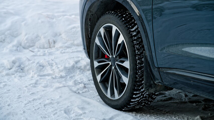 Unrecognizable blue SUV parked on white snow with focus on the alloy rim and black rubber tire tread. Seasonal transportation, climate, and car maintenance background. Photo