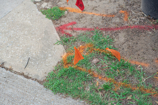 Marked ground area featuring red and orange utility flags and spray painted lines, documenting pre dig mapping procedures used to identify buried cables, ensure safe residential excavation, Texas