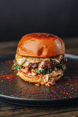 Fresh craft beef burger with cucumbet and chilly flakes on dark plate