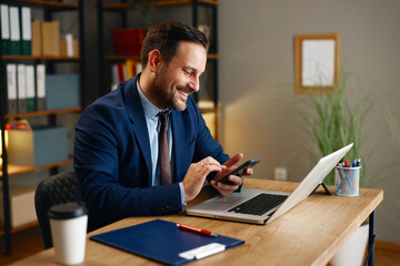 Smiling businessman using smartphone at desk in modern office