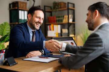 Happy businessmen shaking hands after successful meeting in office