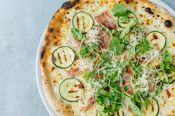 Fresh artisan pizza on a bright background with fresh rucola and ham