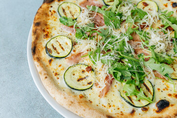 Fresh artisan pizza on a bright background with fresh rucola and ham