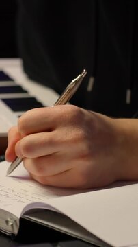 Hands writing lyric songwriting notes in notebook, compact keyboard in backdrop during late night music creation session, vertical
