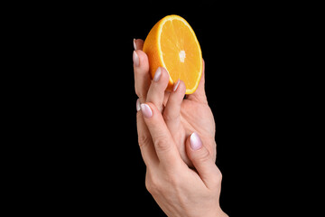 A female hand holding a fresh half orange on a black background. Minimal studio close-up suitable for food, natural ingredients, skincare, hand care, beauty, and wellness concepts.