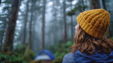 Moody forest adventure scene, person wearing a yellow beanie looks toward a tent barely visible through fog, tall dark trees framing the shot, strong sense of solitude and discover