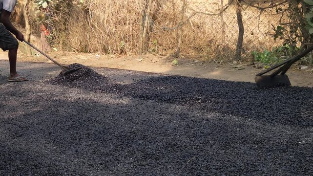 Close-up view of a worker leveling freshly laid bitumen with a rake during road construction, showcasing infrastructure development in a village area.