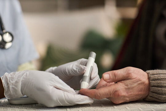 Caucasian senior receiving blood sugar test from medical professional wearing gloves, healthcare worker holding glucometer and pricking finger for diabetes monitoring