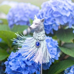 Silver wolf sculpture with blue gem in hydrangeas