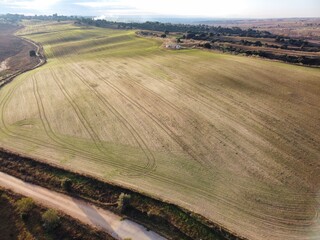 Rolling fields stretch across the landscape with a dirt road winding through them under a clear sky during daylight hours in a rural area