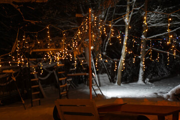 Winter night scene featuring illuminated string lights hanging in a snowy backyard, creating a cozy atmosphere with a playground structure in the background, perfect for festive gatherings