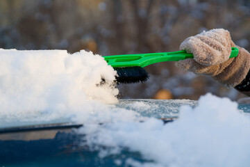Unrecognizable person sweeping fresh heavy snow off a blue automobile after a blizzard. Cold weather transportation and morning cleanup routine. Photo.