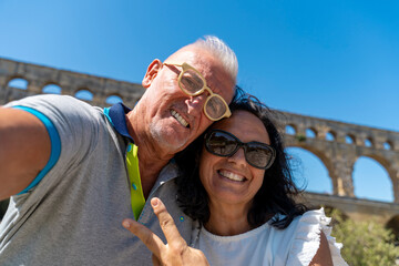 Obraz premium Mature couple smiling and enjoying their vacation, taking a selfie with the pont du gard
