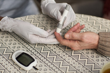 Caucasian senior hand receiving blood glucose test from gloved healthcare worker, medical device and glucometer visible on patterned tablecloth, monitoring diabetes management