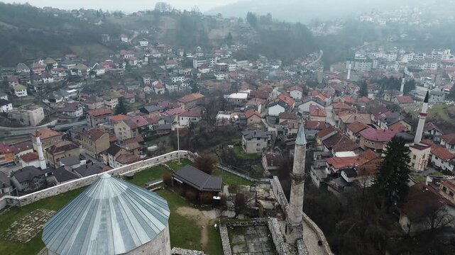 Aerial view of Travnik Fortress overlooking the town and surrounding hills, showing historic stone walls, green courtyards and misty mountain landscape from above. Amazing Bosnia and Herzegovina