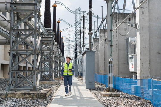Professional electrical engineer walking and inspecting high voltage equipment at power substation, monitoring energy infrastructure for industrial system maintenance and grid reliability.