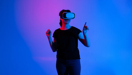 Woman wearing virtual reality headset and interacting with digital environment using hand gestures in futuristic neon blue and purple studio lighting