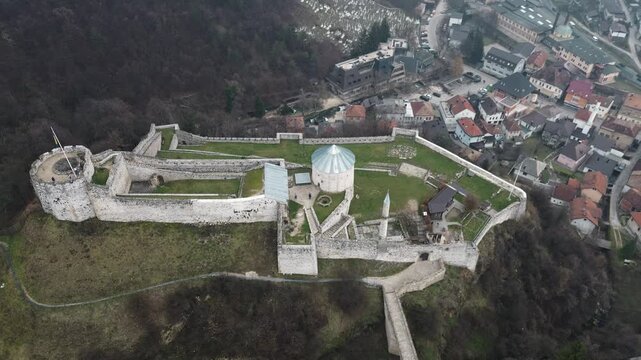 Aerial view of Travnik Fortress overlooking the town and surrounding hills, showing historic stone walls, green courtyards and misty mountain landscape from above. Amazing Bosnia and Herzegovina