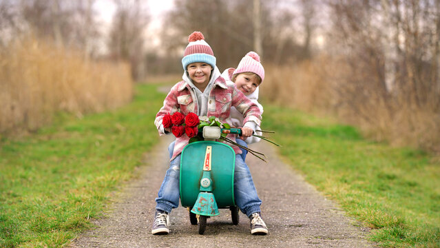 happy boy and girl riding a pedal scooter wit a bouquet of red roses